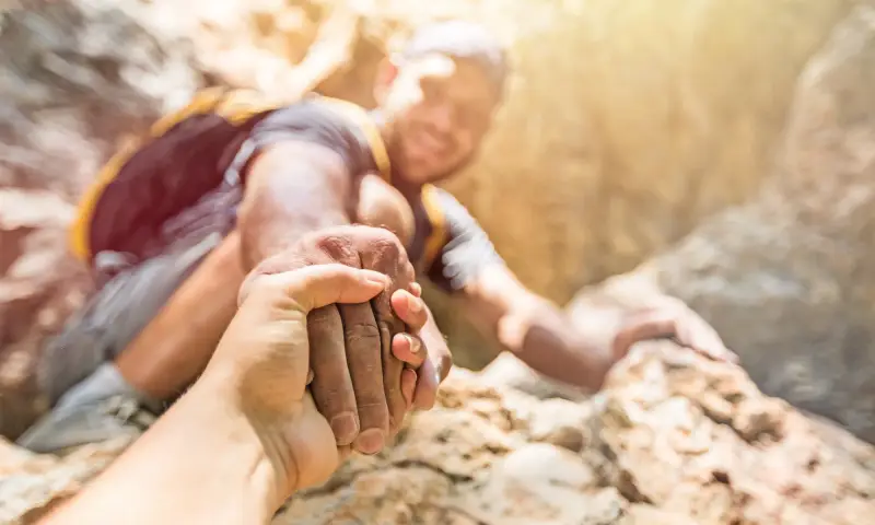 Eine Hand hilft einer anderen beim Klettern über einen Felsen